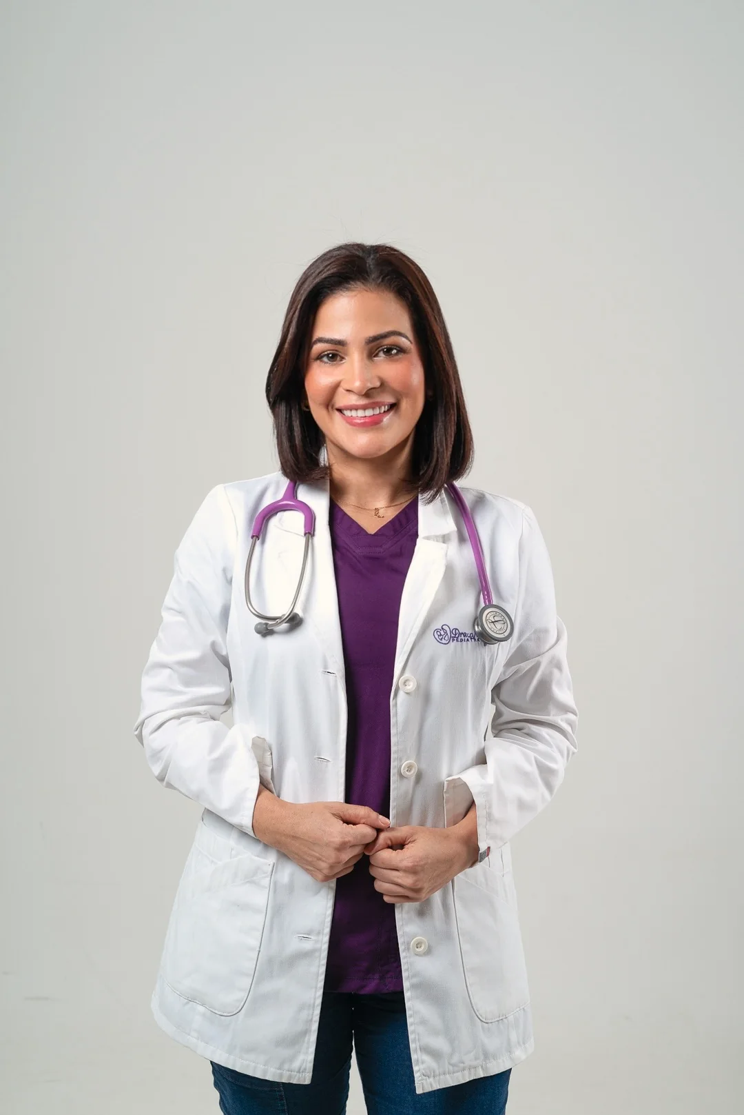 La doctora con bata, sonriente, con las manos juntas